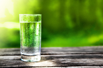 Glass Of Crystal Clear Mineral Water On Old Wooden Table On Background Of Nature Or Forest. Concept Of Healthy Diet Or Problem Of Environmental Pollution.