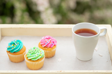 Bright cakes. Cupcakes with a cup of coffee or tea on a tray with a colorful bright background, a sunny morning and a bright mood. spring background