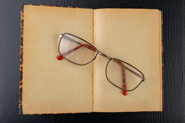 Old book and glasses on a dark wooden table. Forgotten publishing in binding from several decades...