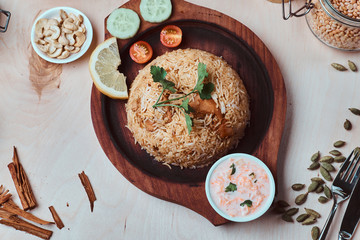 Traditional dish with rice, cashew nuts, sauce, lemon, vegetables and coriander leaf on wooden tray.
