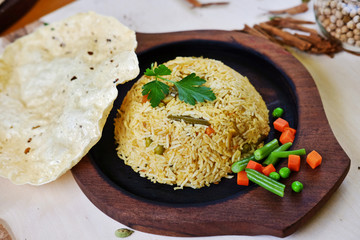 Traditional indian curry rice with parsley leaf, popadom and vegetables on wooden plate.