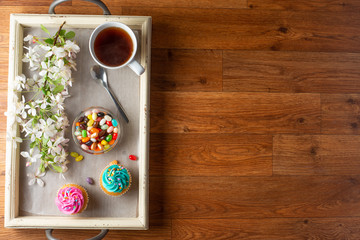 Bright cakes. Cupcakes with a cup of coffee or tea on a tray with a blossoming twig on a wooden background, flat lay
