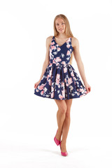 Beautiful young blonde woman in dark blue dress with floral print isolated on white background