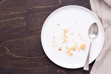 Empty white plate with crumbs on dark wooden background, top view