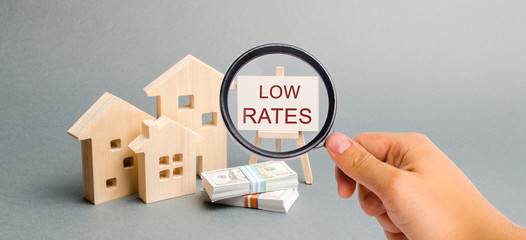 A magnifying glass is looking at a poster with the word Low rates and wooden house. The concept of...