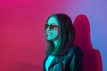 Fashioned girl in leather jacket in dark glasses in pink anf blue  neon lights background. 