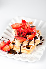Belgium waffers with sugar powder, strawberries and chocolate on ceramic plate on white table.