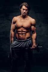 Fototapeta na wymiar Beautiful young bodybuilder is posing with dumbbell. He has naked torso.