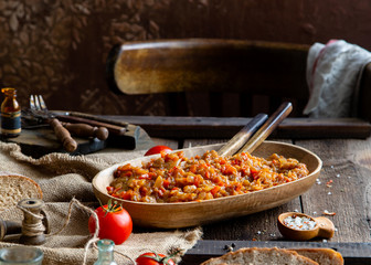 Homemade tasty orange vegetable caviar, ratatouille or ragout in oval wooden dish on rustic brown table