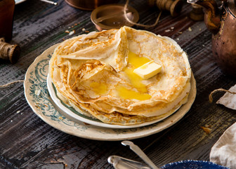 Homemade crepes with melted butter on vintage plate with green ornament stand on rustic grey table