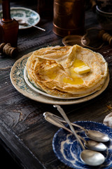 Homemade crepes with melted butter on vintage plate with green ornament stand on rustic grey table