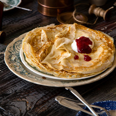 Homemade crepes with sour cream and red jam on vintage plate with green floral ornament stand on rustic table