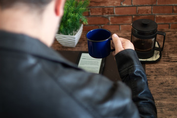 Homem sentado de jaqueta desfocado tomando café em xícara azul antiga lendo e-book