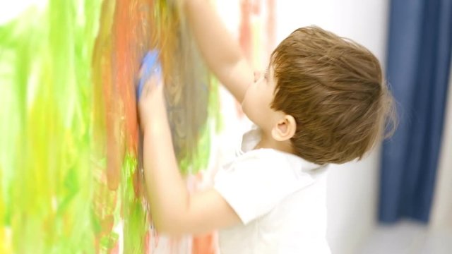 Close up of happy little child making colorful handsprint on the white wall with mother together. Slow motion