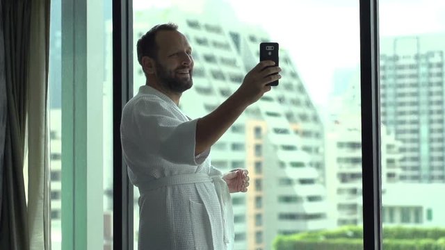 Happy man wearing bathrobe and doing selfies on smartphone, slow motion shot at 120fps