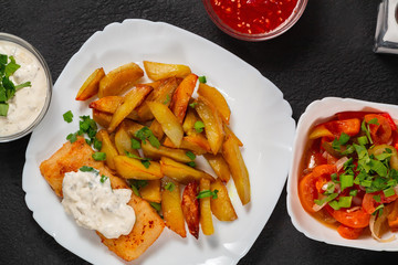 Fried fish and chips on a white plate on black the kitchen table with tomato sauce, tartar sauce...