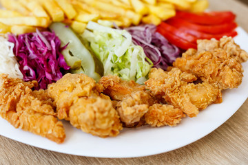 Chicken wings on the plate with french fries, tomatoes, onion, pickles and cabbage salad on a wooden background.