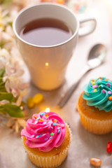 Obraz na płótnie Canvas Bright cakes. Cupcakes with a cup of coffee or tea and color dots on a tray with a flowering branch and a luminous garland on a white background. Morning mood, spring background