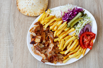Chiken Doner Kebab on the plate with bread, french fries, tomatoes, onion, pickles and salad on a wooden background. Grilled chicken meat with vegetables.