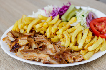 Chiken Doner Kebab on the plate with french fries, tomatoes, onion, pickles and salad on a wooden background. Grilled chicken meat with vegetables.