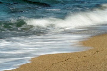 Detail view of a wave, which runs out on a sandy beach, the blue color of the sky is reflected in the water, some washed-up seagrass on the sand, water movement in decent long exposure -Caribbean