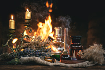 Alchemist or witch doctor table. Magic potion bottles and dried herbs on a table on a burning fire...