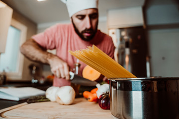 .Young man cooking at home, wearing a white chef hat while maintaining healthy recipes with a variety of vegetables. Selective focus. Lifestyle.