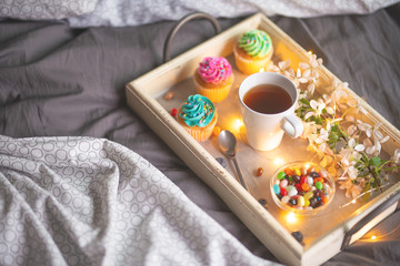 Morning breakfast in bed. Wooden tray with coffee or tea and cupcakes. Gray bedspread in the interior of a hotel room. Copy space
