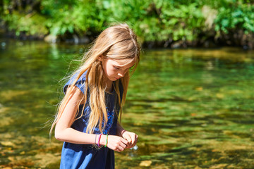 Child cute blond girl playing in the creek. Girl walking in forest stream, looking for pebbles and exploring nature. Summer children fun. Children summer activities