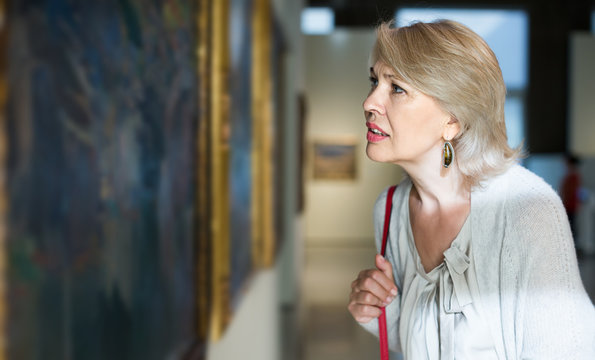 Mature woman standing in art museum near the painting in baguette