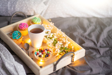 Morning breakfast in bed. Wooden tray with coffee or tea with bright cakes. Gray cover of the hotel...