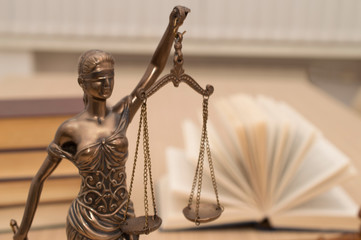 statue of justice on wooden table against the background of an open book.