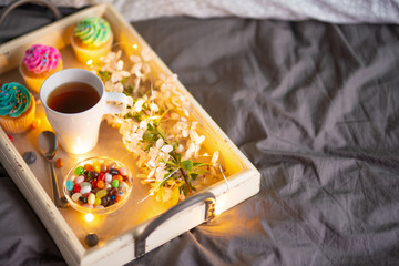 Morning breakfast in bed. Wooden tray with coffee or tea and cupcakes. Gray bedspread in the interior of a hotel room. Copy space
