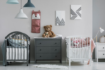 Pink organizer on wall of trendy baby bedroom with two cribs and chest of drawers