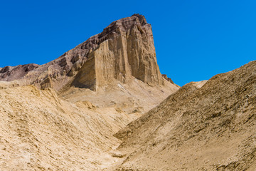 A high desert peak with sheer cliffs rises above a barren, golden desert landscape - Golden Canyon in Death Valley National Park