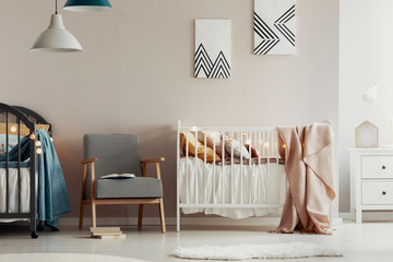 Fashionable retro armchair between two wooden cribs in cute twins nursery - obrazy, fototapety, plakaty