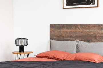 Bed with wooden headboard, coral sheets and black industrial lamp