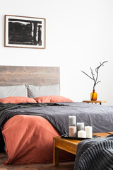 Vertical shot of wooden bed with linen bedclothes, artwork and orange vase