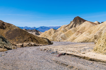 A dry rocky riverbed curves through a barren desert landscape of colorful badlands and peaks in Death Valley National Park
