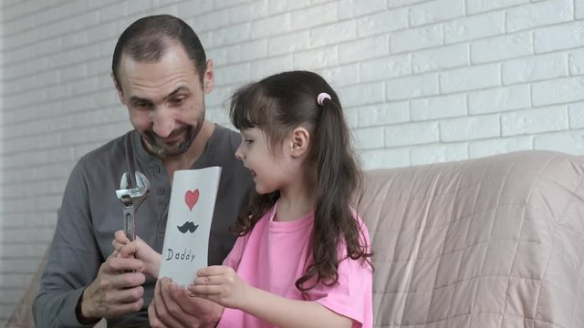 Father's day. A cute little girl gives her dad a postcard and a monkey wrench.