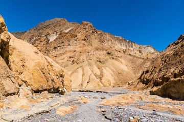 Fototapeta na wymiar A canyon with a dry riverbed of gray rock contrasted with golden cliffs and peaks - Gower Gulch, Death Valley National Park