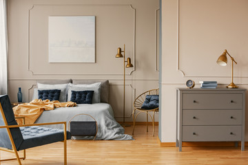 Elegant bedroom interior with king size bed, painting on the wall and grey commode