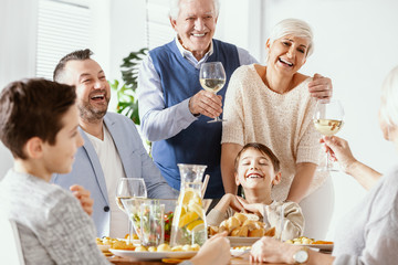 Smiling grandfather drinking wine during family dinner with happy boy and his parents