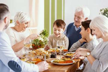 Smiling boy eating dinner with parents, happy grandmother and grandfather
