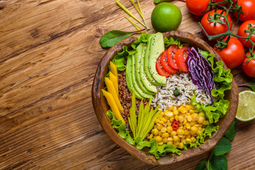 Buddha bowl with chickpea, avocado, wild rice, quinoa seeds, bell pepper, tomatoes, greens, cabbage, lettuce on old wooden table. Top view with copy space. Healthy vegan food.
