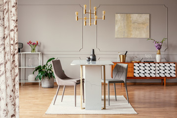 Stylish gray dining chairs by an elegant marble table with golden frame in a classy apartment room interior with gray walls