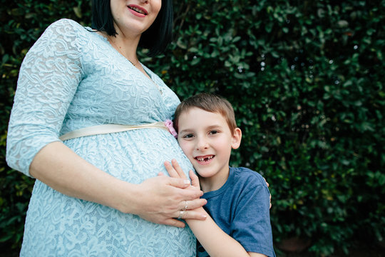 Young boy with a toothless smile puts hand on mom's pregnant belly