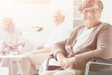Fototapeta premium Smiling grandmother in the wheelchair in the nursing house and senior people