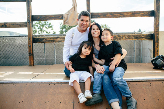 Family of four sits on half pipe while smiling for camera