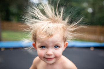 Toddler girl on trampoline with wild static hair